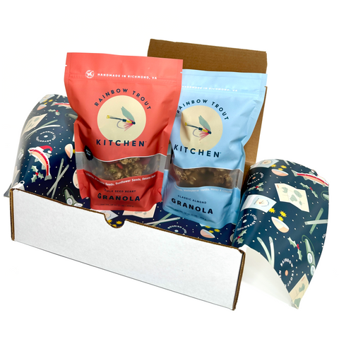 A gift box containing two bags of granola, one labeled 'Almond' and the other 'Triple Seed Berry', with festive holiday packaging.