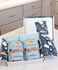 Box of granola packages with decorative packaging on a kitchen counter.